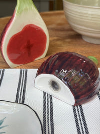 Ceramic salt shaker with red and white design on a striped cloth, with a cut fig and ceramic bowl in the background.