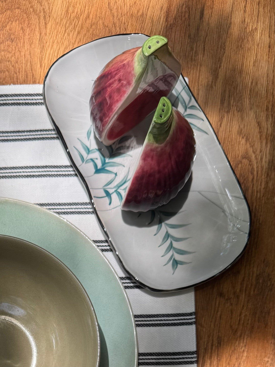 Sliced fig on a decorative plate with a bowl and striped place mat in the foreground.