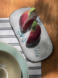 Sliced fig on a decorative plate with a bowl and striped place mat in the foreground.