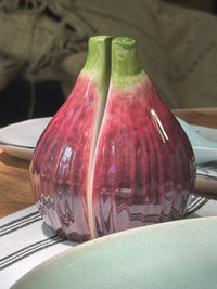 Ceramic salt and pepper shakers shaped like a fig on a table.