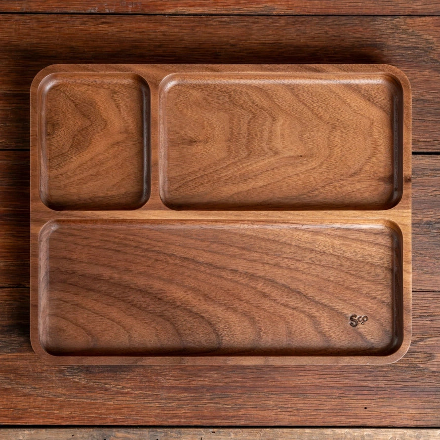 A three-compartment wooden serving tray with a rich walnut wood grain, shown from a top-down view on a matching wooden surface.