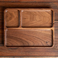 A three-compartment wooden serving tray with a rich walnut wood grain, shown from a top-down view on a matching wooden surface.