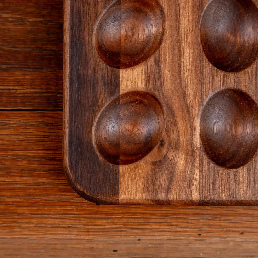 Close-up of a dark brown wooden board with four raised oval cavities, photographed on a matching wood surface.