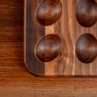 Close-up of a dark brown wooden board with four raised oval cavities, photographed on a matching wood surface.