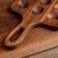 A close-up of a dark brown wooden serving board with a handle and circular recessed details, resting on a matching wooden surface.