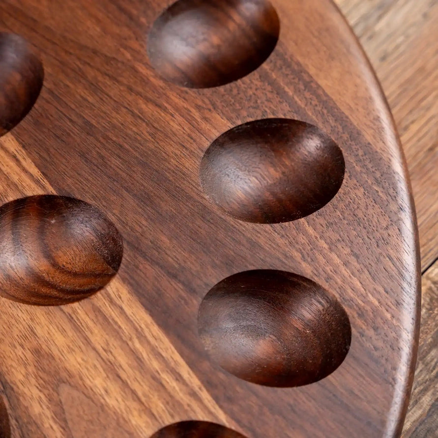 Close-up of a dark brown wooden board with oval recessed pockets, showing visible wood grain and a portion of a matching wooden surface around it.