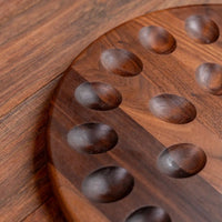 A close-up of a round wooden board with carved oval indentations, photographed on a matching wood surface.