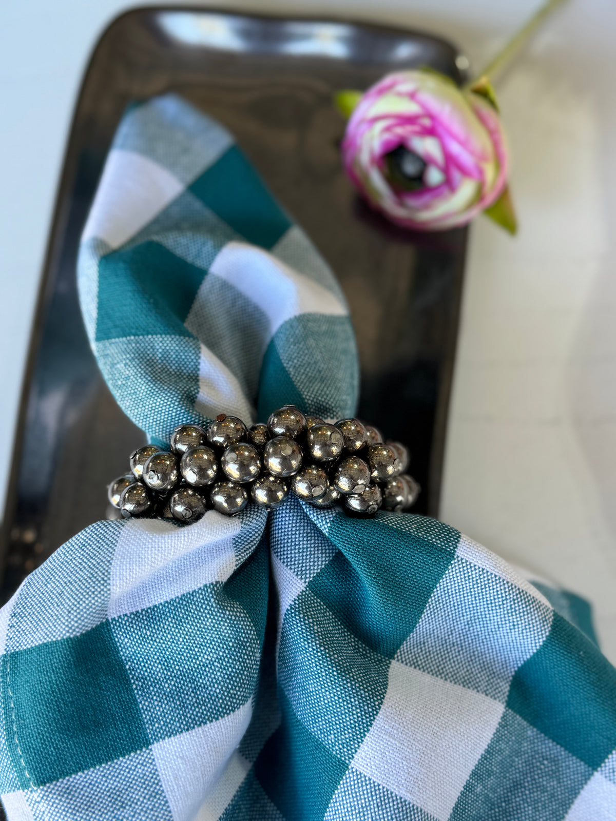 Teal and white checkered napkin with a silver napkin ring on a black surface.