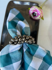 Teal and white checkered napkin with a silver napkin ring on a black surface.