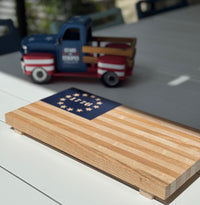 Wooden block with American flag design in front of a toy truck on a light surface.