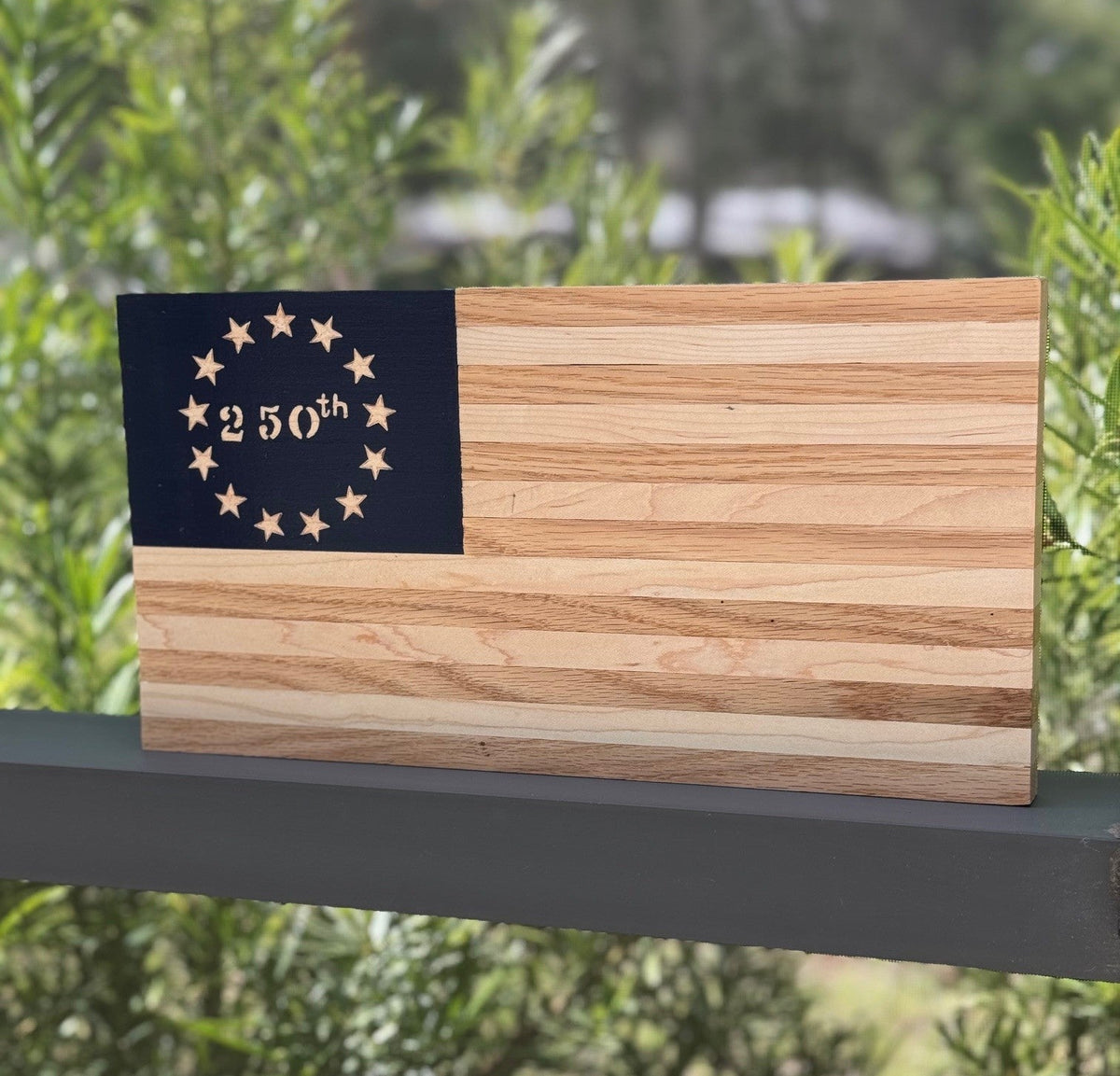 Wooden flag with '250th' design on a metal surface with a natural background