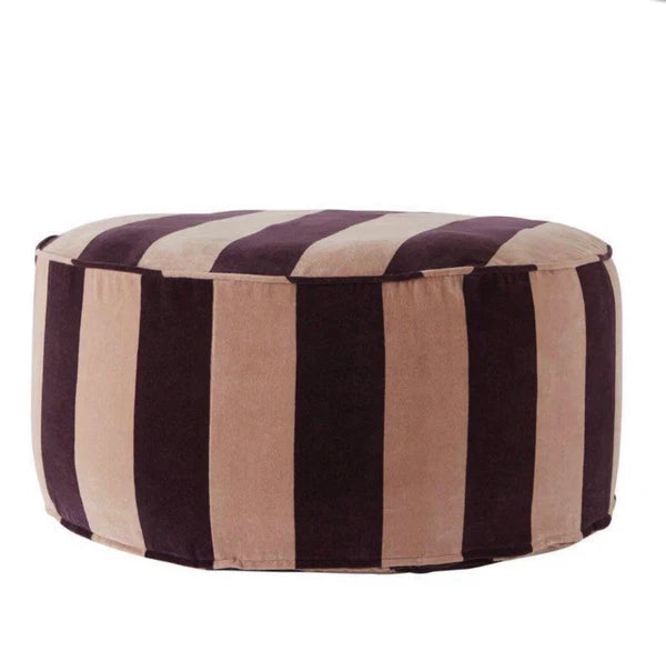 A striped pouf in blush and maroon colors with a black leather handle.