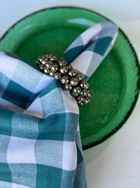 Green plate with a checkered cloth and decorative napkin ring on a white background