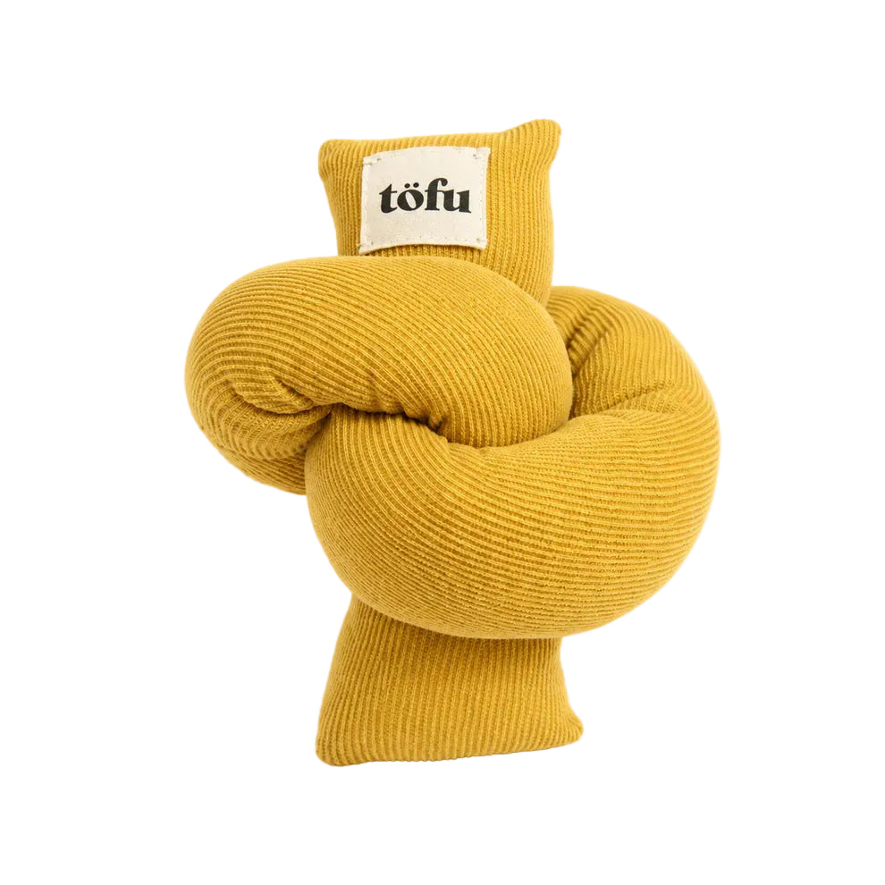 A yellow ribbed fabric dog toy shaped like a twisted knot, featuring a small cream-colored sewn-on label with the brand name 'töfu' printed in black.