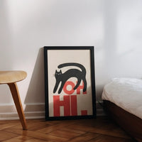 Framed artwork with a black cat and red text on a white wall.