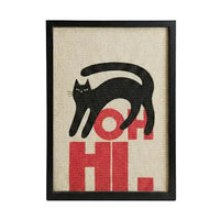 Framed wall art featuring a black cat silhouette walking over bold red letters spelling 'OH HI.' on a beige woven-texture background, shown in a black frame against a light gray studio backdrop.