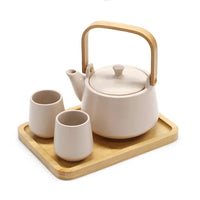 Ceramic teapot with wooden handle and two cups on a wooden tray