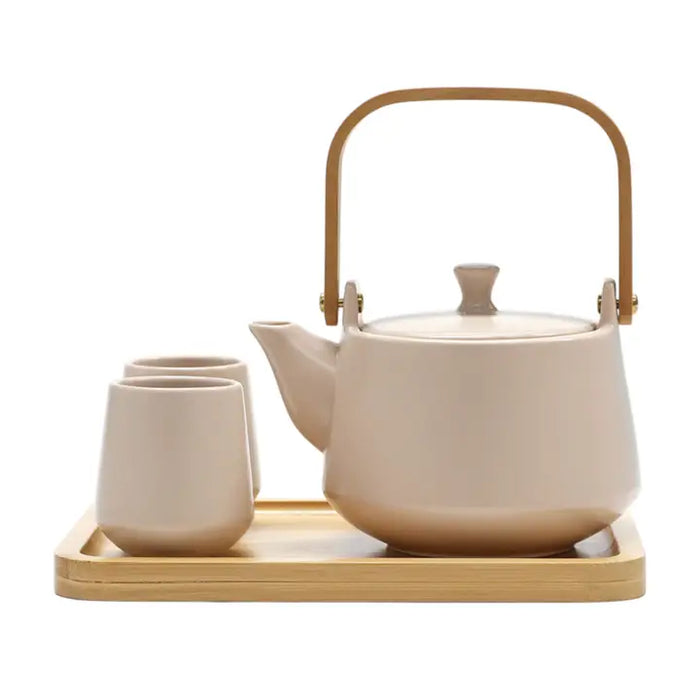 Ceramic teapot with wooden handle and two matching cups on a wooden tray against a white background