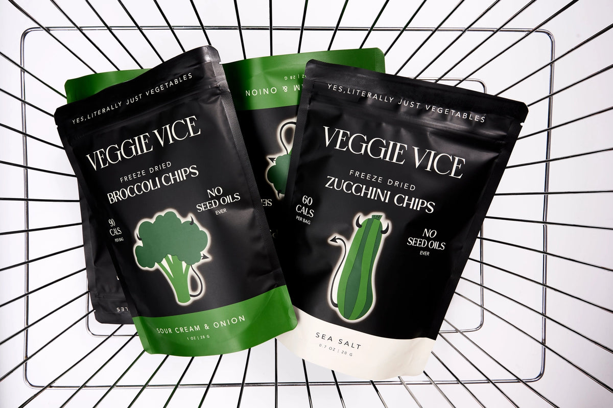 Three packages of Veggie Vice freeze-dried vegetable chips on a grid background