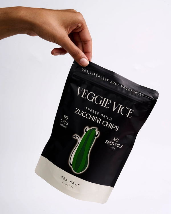 Hand holding a black Veggie Vice zucchini chips package on a white background