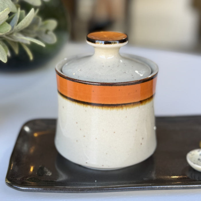 Ceramic container with an orange band on a tray, blurred background