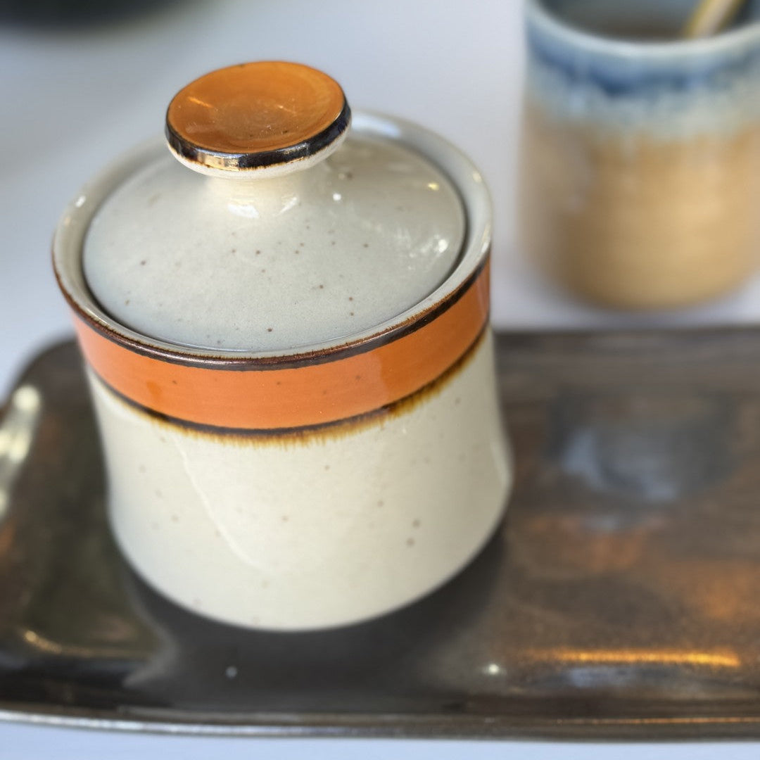 Ceramic container with an orange band and gold lid on a tray