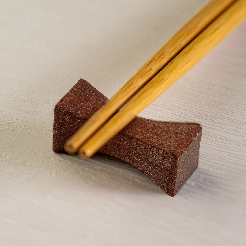 Wooden chopsticks resting on a brown wooden block against a light background