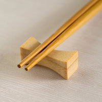 Wooden chopstick rest with two wooden chopsticks on a light brown surface