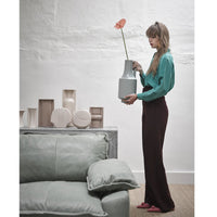 group of earthenware flowervases behind sofa and woman holding green vase