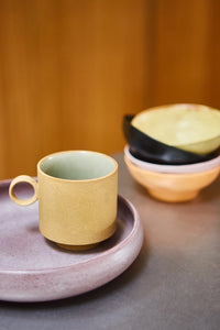 purple plate, yellow mug with an ear an a yellow, black, pink and orange bowl in a stack