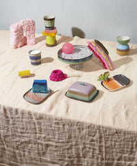 retro style small stoneware coffee mug in brown, aqua and lavender colors on a table with a linen table cloth and colorful plates