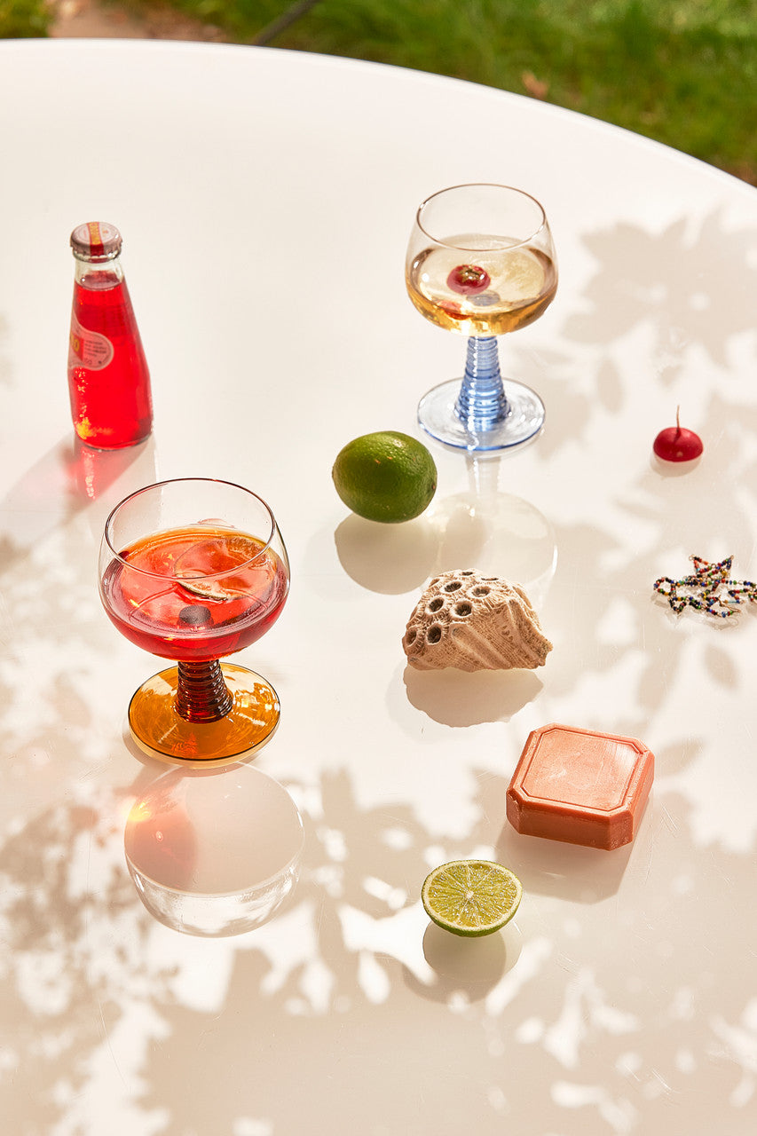 retro style wine glass with a low red colored swirled stem on a table with objects