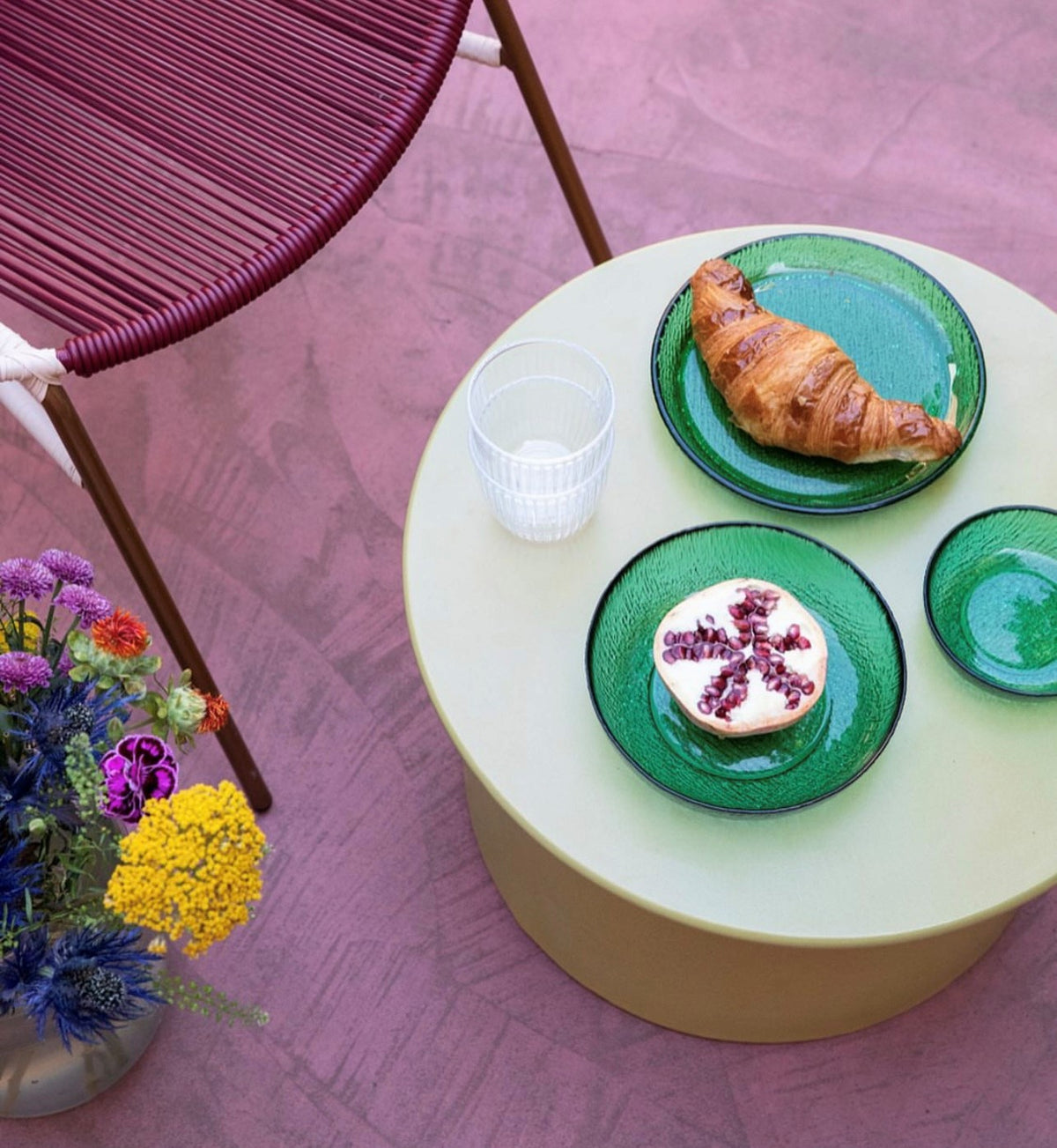 green stoneware side table on a purple floor with 3 green glass plates with fruit and a croissant