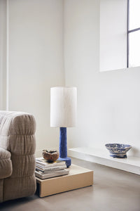  sand colored wooden low plateau table next to a linen couch with a blue table lamp