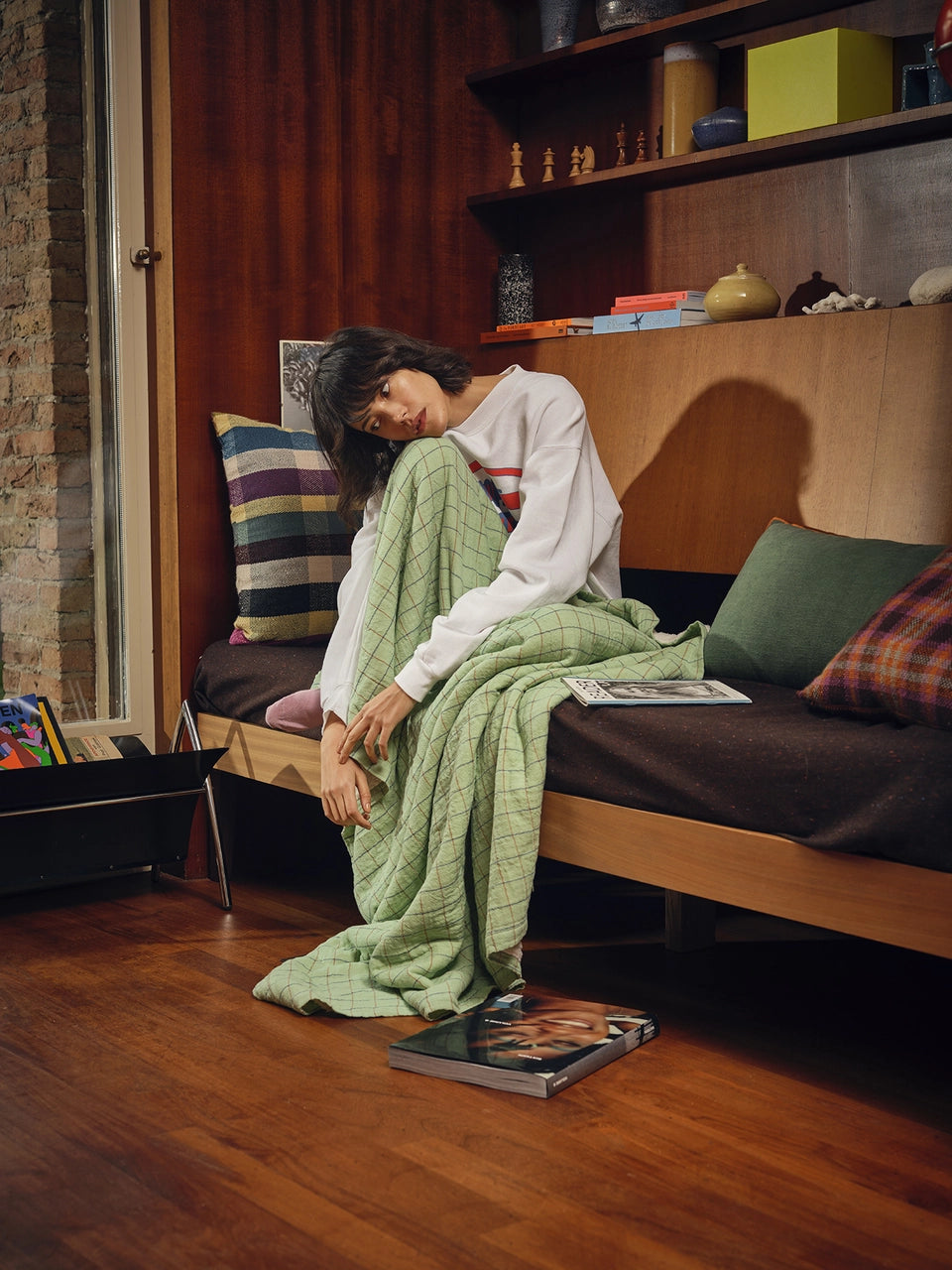 woman with a green throw blanket sitting on a sofa next to a retro style multicolored cotton throw pillow