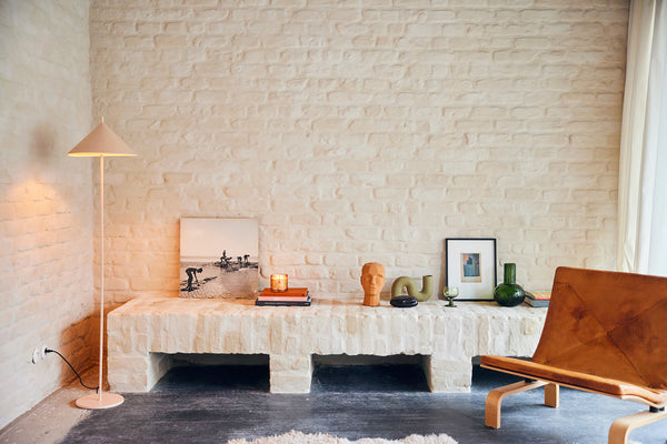 metal triangle floor lamp in blush in living room with white painted brick exposed wall 