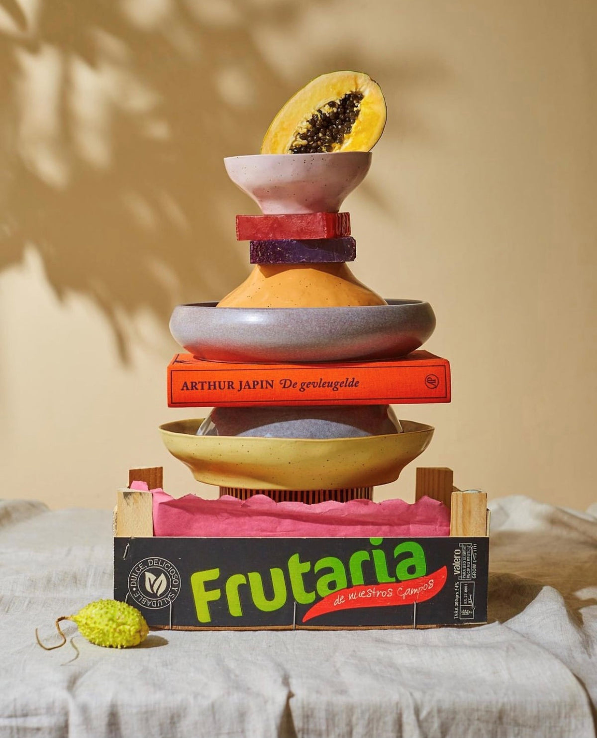 stack of bold and basic ceramics with books in a fruit crate on a table