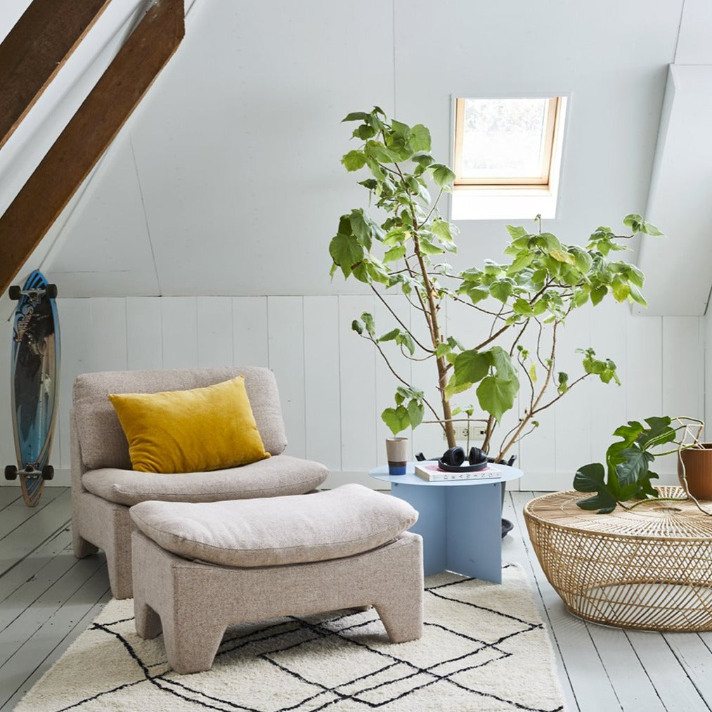 boucle lounge chair with ottoman in pink next to a blue side table and a big green plant behind the chair