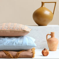 blush colored pillow with silver stitches, blue pillow with texture and throw blanket in a golden brown color with textured tufted lines