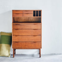 brown secretary cabinet with drawers and a hand woven woolen lumbar pillow standing up 