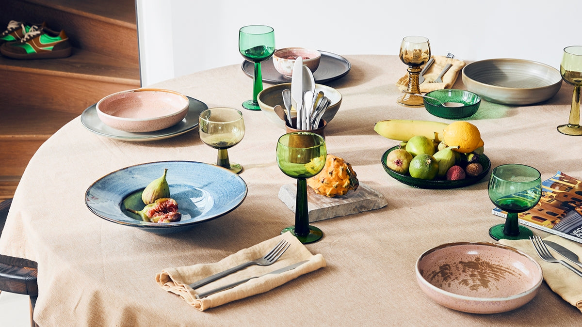 table setting with blue and pink pasta plates and high and low stem green wine glasses