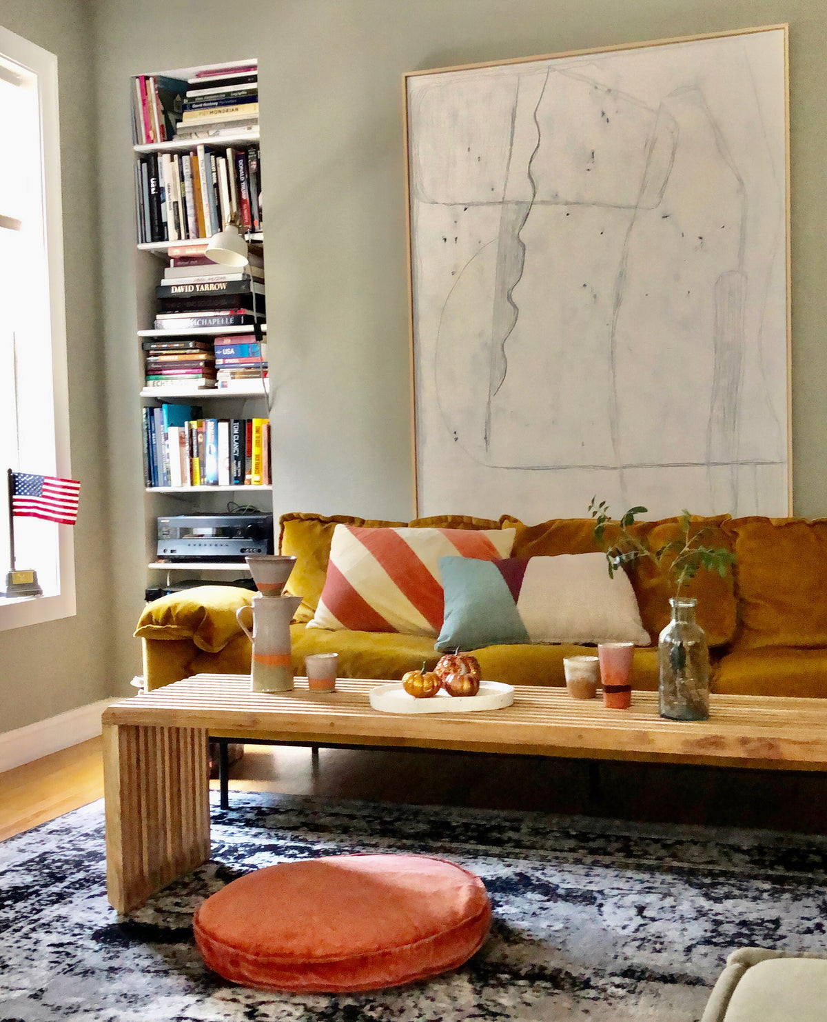 living room with large abstract white painting, ochre sofa, wooden bench and colorful home decor